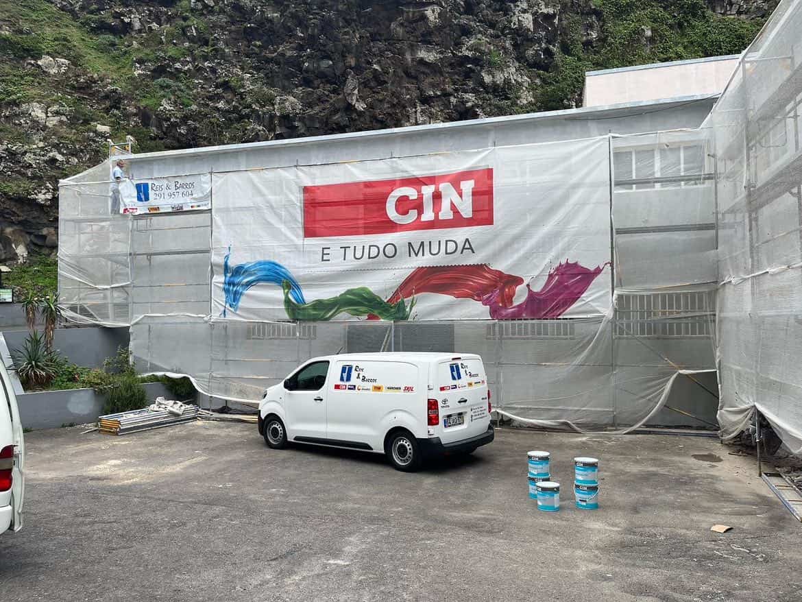 Obra exterior com andaimes, carrinha Reis & Barros e lona CIN